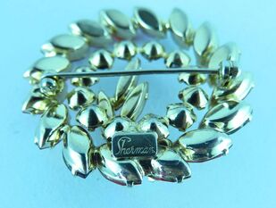 Reverse side of Sherman brooch with circular design and Sherman mark on blue background