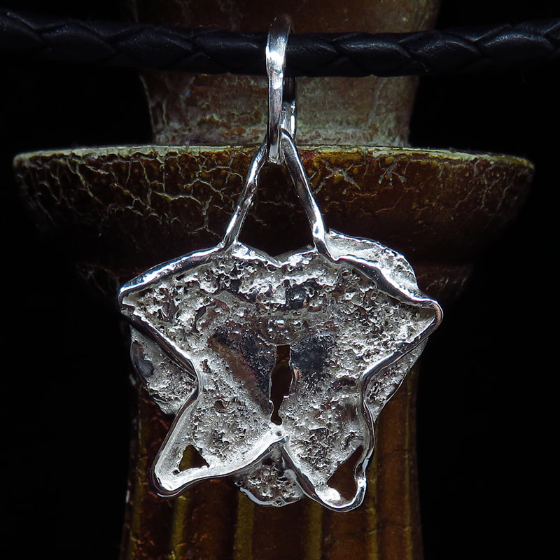 Sterling silver pendant handmade star-shape over heart with raw texture suspended from braided black leather against antique backgroundPicture