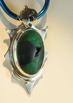 Handmade sterling silver pendant with green and black malachite bezel-set cabochon with ornamental bail and star-shaped background on pale cream background